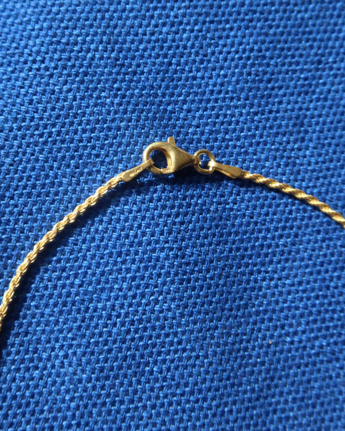 Close-up of a gold chain necklace lobster claw clasp on a textured blue fabric background.