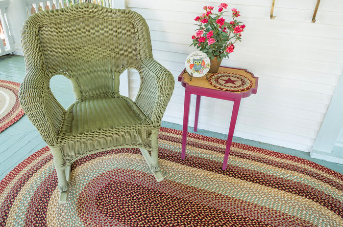 Braided jute rug with Burgundy, Gray and Cream braids below a green wicker chair and side table.