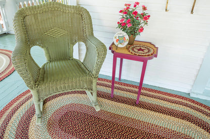Braided jute rug with Burgundy, Gray and Cream braids below a green wicker chair and side table.