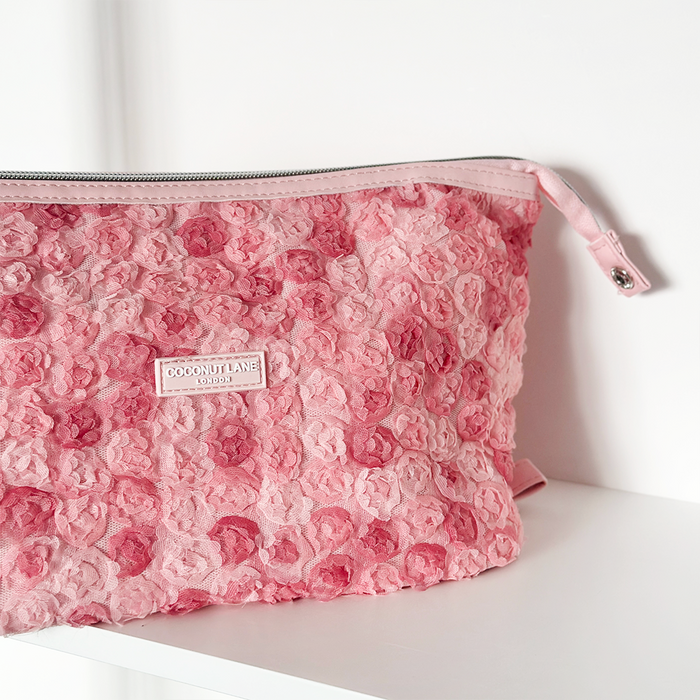 Expandable pink lace-textured makeup bag with zipper on a white shelf.