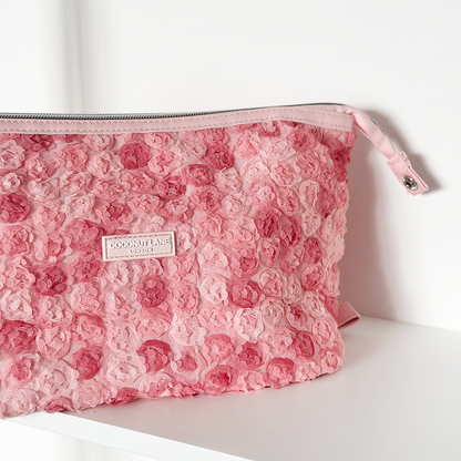 Expandable pink lace-textured makeup bag with zipper on a white shelf.