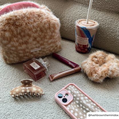 Fawn makeup products on a boucle sofa, makeup bag, claw clip, scrunchie and phone case all match