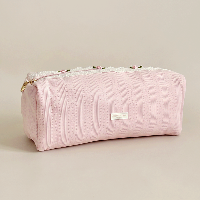 Pink pointelle fabric hair tool bag with Coconut Lane logo badge. White lace trim detailing.