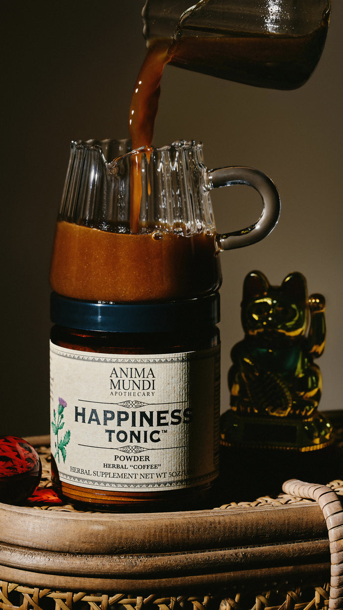 Anima Mundi Happiness Tonic being poured into a glass jar with a cat figurine in the background.
