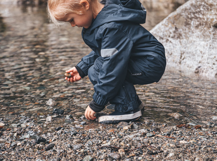 Child playing in rain wearing navy hard-shell jacket by KidORCA