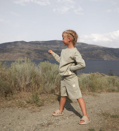 Child wearing sage green french terry shorts – side view with elastic waist