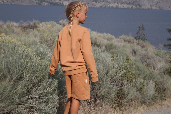 Child wearing sandstone beige french terry shorts – side view with elastic waistband