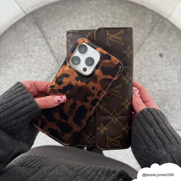 Hands holding a leopard print phone case and brown Louis Vuitton wallet, wearing a dark grey sweater.