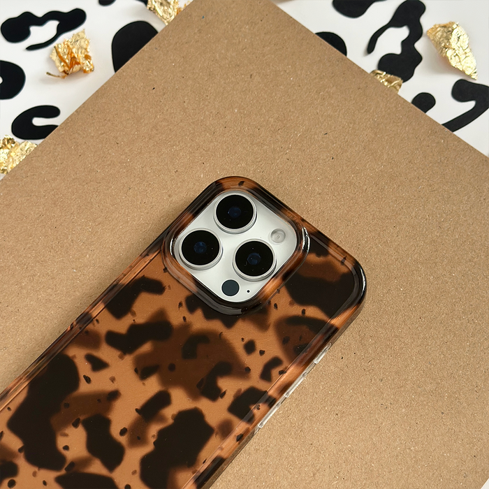 Leopard tortoiseshell phone case by Coconut Lane displayed on cardboard, with black and white abstract accents nearby.