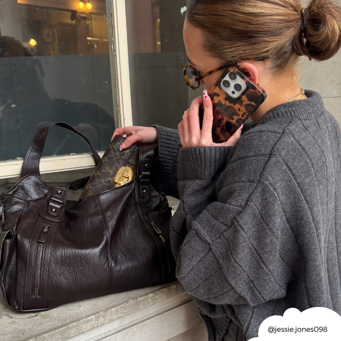 Woman in gray sweater holds a Coconut Lane phone case with leopard tort pattern, reaching into a brown leather bag.