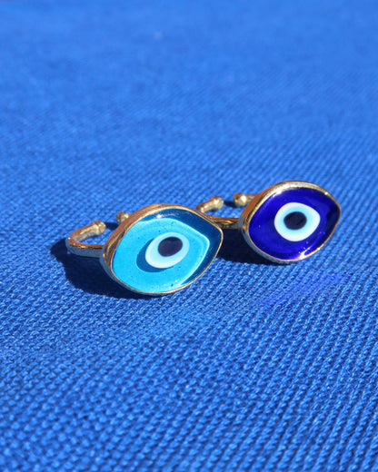 Two evil eye rings, one with a light blue Murano glass evil eye design and a gold band, and one with a dark blue Murano glass evil eye and gold band made in Greece; Greek evil eye jewelry rings