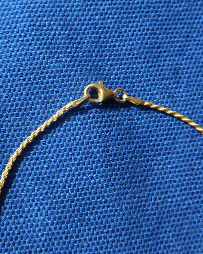 Close-up of a gold chain necklace lobster claw clasp on a textured blue fabric background.