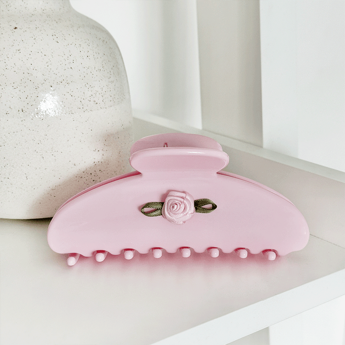 Pink hair claw clip with a small rose embellishment and green ribbon accent.