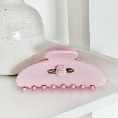 Pink hair claw clip with a small rose embellishment and green ribbon accent.