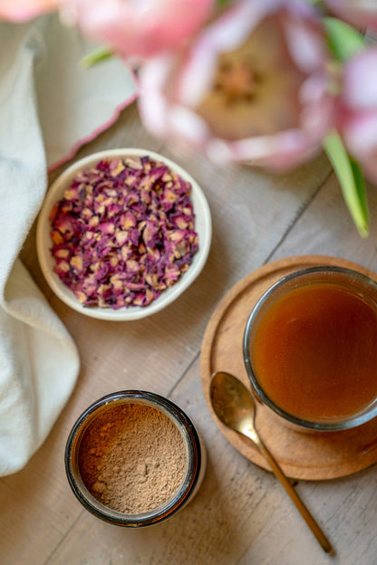 Tea-making setup with dried flowers, tea leaves, and a cup of tea on a wooden surface.