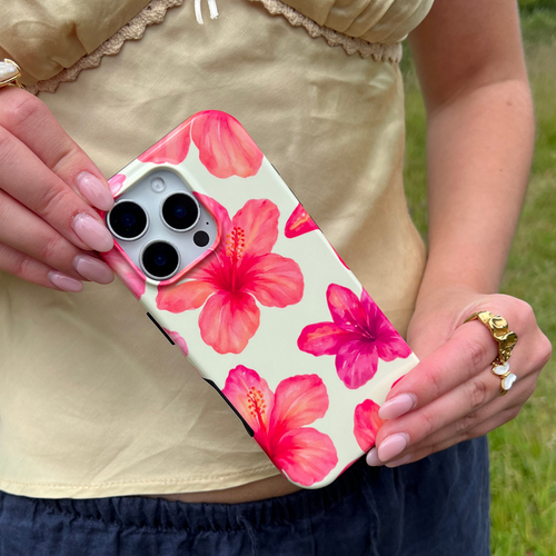 Butter yellow phone case with hibiscus pattern held in hand with manicured nails and a gold ring.