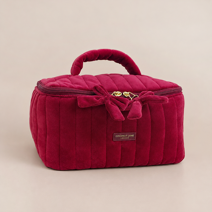 Burgundy velvet cosmetic bag with a quilted design, top handle, bow detail, and gold-tone hardware.