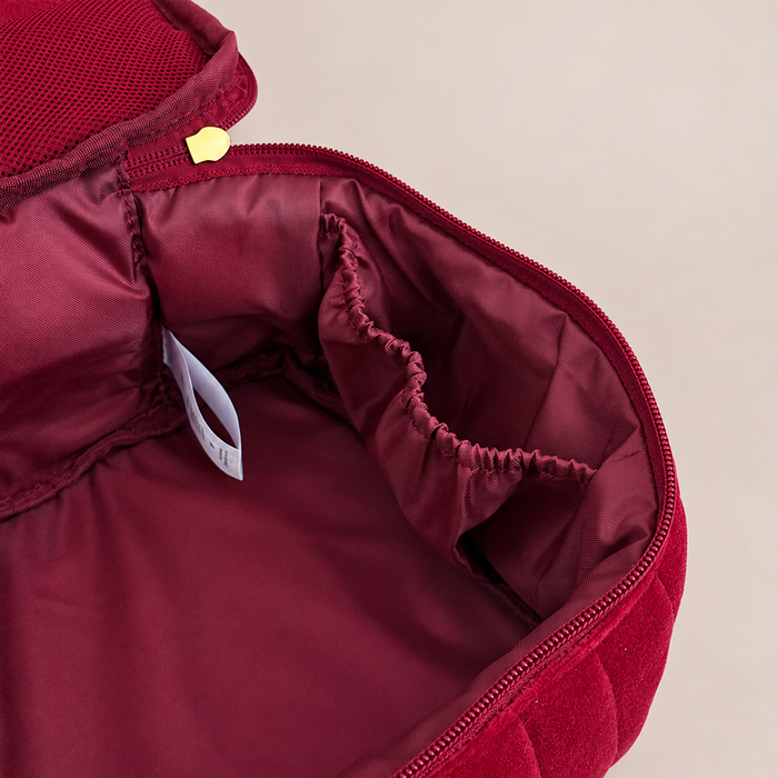 Close-up of the interior of a burgundy zippered bag or organizer, showing a padded lining, elastic pocket, zipper pull, and a small white tag on a light beige background.