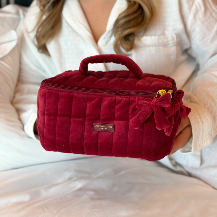 girl in white Pjs holds Burgundy velvet cosmetic bag with a quilted design, top handle, bow detail, and gold-tone hardware.